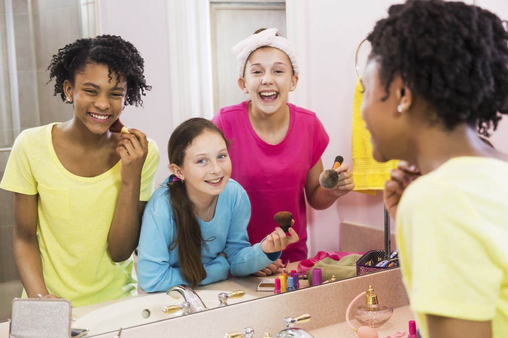 Three girls at sleepover looking into mirror in bathroom