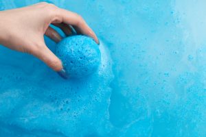 women placing blue bath bomb into blue bath water
