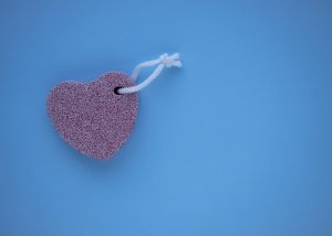Pink heart shaped pumice stone for feet and elbows skin care on isolated a blue background