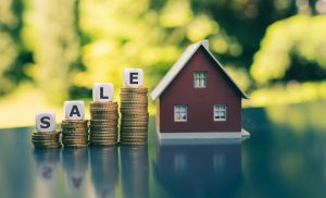 Model of house with coins and blocks spelling the word "sale"