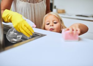 mother and her little daughter cleaning a kitchen surface together at home
