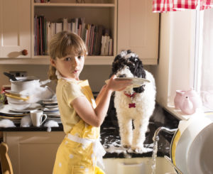 little girl in kitchen washing dishes with the help of her dog