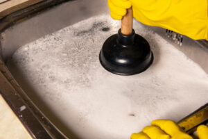 rubber gloves and plunger in sink