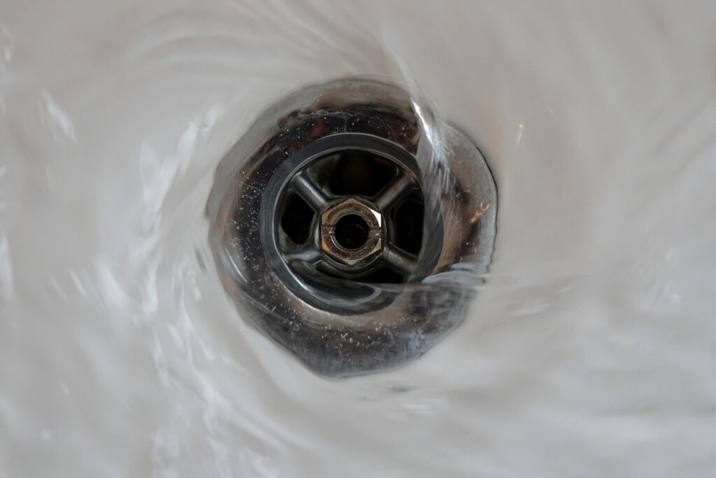 Water swirls rapidly around a metal sink drain and rushes down, clearly showing how Hydro Jetting removes blockages more effectively than traditional snaking.