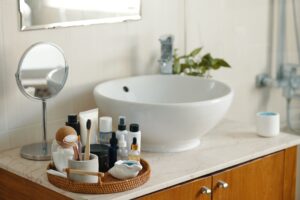 A bathroom countertop displays a round white sink, a small mirror, and a wicker tray with toiletries for easy access and simple plumbing care.