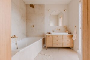 Modern bathroom featuring built-in tub—check for wear to know when to replace. Wooden vanity, double sinks, round mirror, neutral tones.