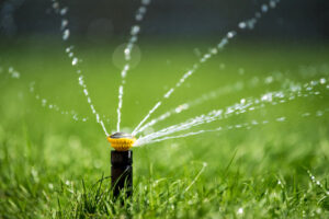 A lawn sprinkler actively waters green grass with multiple streams on a sunny day, helping conserve water in Orange County.
