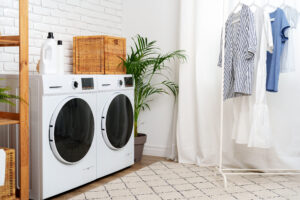 Stay prepared for burst pipes in this bright, clean laundry room with washer, dryer, wicker baskets, detergent, plant, and hanging clothes.